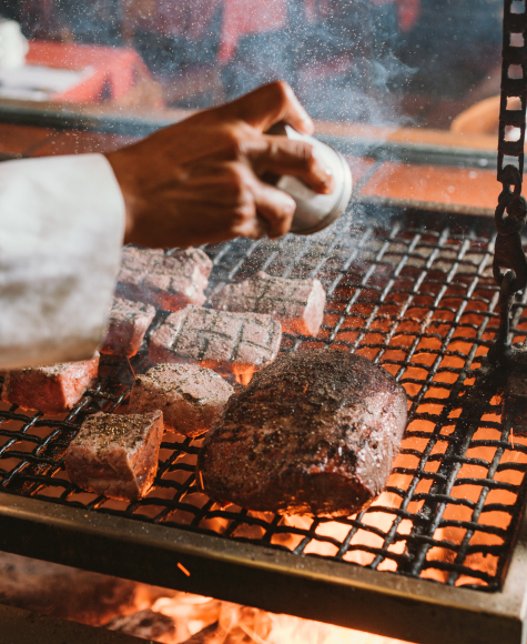 A close up of a chef salting a tri-tip roast over an open flame